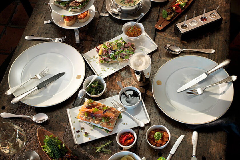 Stilvoll gedeckter Tisch mit hochwertigem Silberbesteck, weißen Tellern und feinen Speisen für elegante Tischkultur.